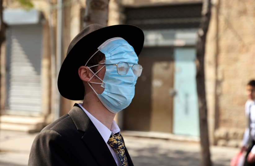 An ultra-Orthodox man wears three masks over his face while celebrating Purim amid coronavirus disease (COVID-19) restrictions in Jerusalem February 28, 2021  (photo credit: RONEN ZVULUN/REUTERS)