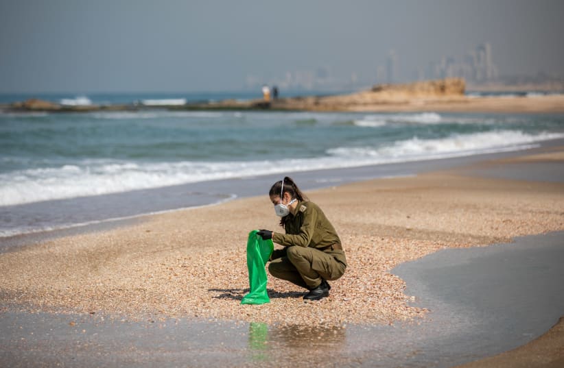 Israeli soldiers clean tar off the Palmachim beach following an offshore oil spill which drenched most of the Israeli coastline, February 22, 2021 (photo credit: YONATAN SINDEL/FLASH 90)