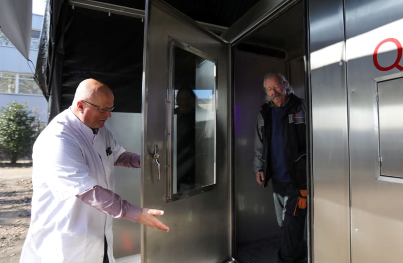 Peter van Wees opens the door so John Moritz can exit the quick breath analyzer cabin that tests for the coronavirus disease (COVID-19) at a testing location in Amsterdam, Netherlands March 1, 2021. (photo credit: REUTERS/EVA PLEVIER)