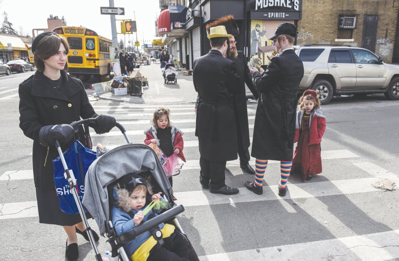 A FAMILY pauses in the street as people celebrate Purim in Brooklyn earlier this month. (photo credit: STEPHANIE KEITH/REUTERS)