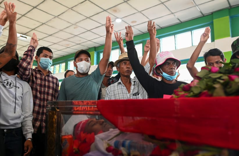 People flash a three-finger salute in front of a casket with a body of a victim who was shot dead during the anti-coup protest, in a cemetery at the outskirts of Yangon, Myanmar, March 5, 2021.  (photo credit: STRINGER/ REUTERS)