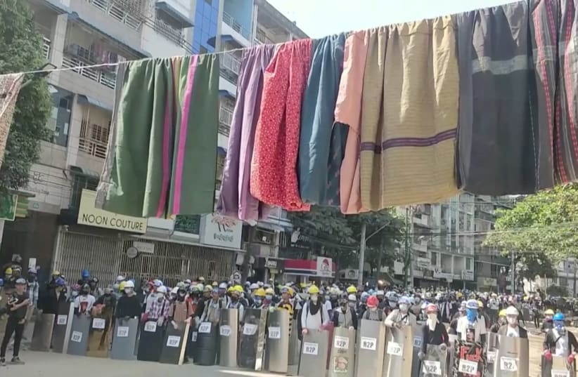 Traditional clothes hang on a rope as protesters holding shields stand in line in the background during a protest against the military coup in Yangon, Myanmar March 6, 2021 in this still image obtained by Reuters from a video. (photo credit: REUTERS)
