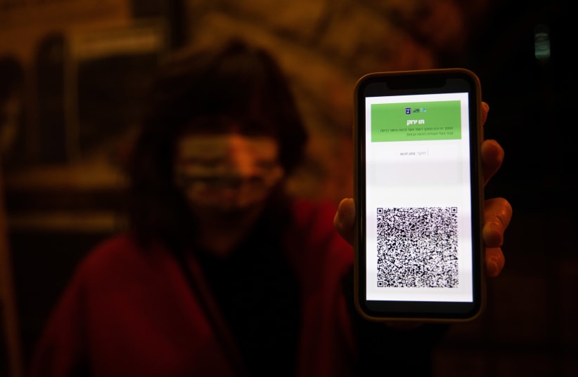 A woman shows her green passport at the Khan theater in Jerusalem on February 23, 2021. (photo credit: YONATAN SINDEL/FLASH90)
