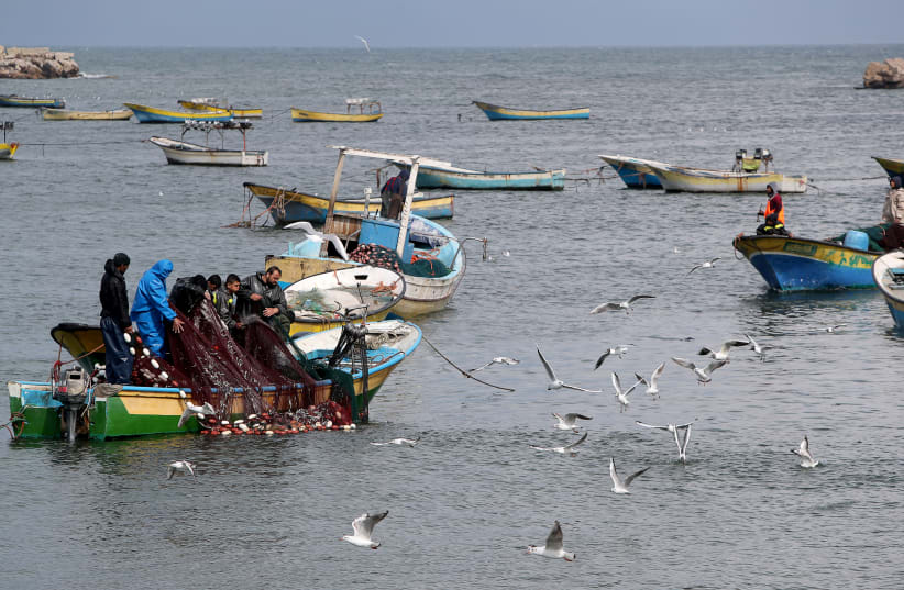Palestinian fishermen riding a boat cast their net as birds fly off the coast of Gaza City February 19, 2020 (photo credit: REUTERS/MOHAMMED SALEM)