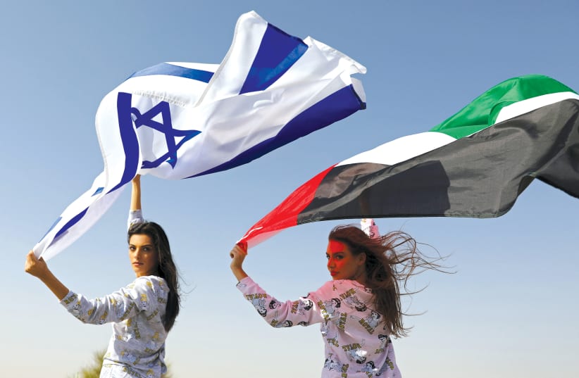 Israeli model May Tager, holding an Israeli flag, poses with Dubai model Anastasia, holding an Emirati flag, during a photo shoot for FIX’s Princess Collection in Dubai in September, 2020 (photo credit: CHRISTOPHER PIKE/REUTERS)