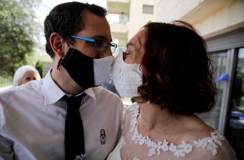 An illustrative photograph: Bride Osnat Baron and groom Yaniv Jenger kissing through their masks during their wedding party with a limited number of guests in the garden of a private house in Jerusalem on April 27, 2020 (photo credit: RONEN ZVULUN/ REURERS)