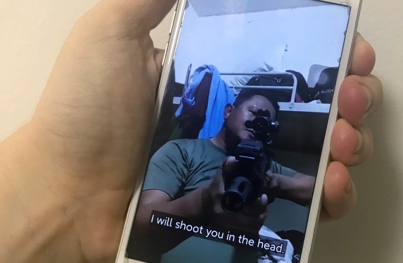 A mobile phone shows a picture of a Myanmar man in an army shirt threatening to shoot anti-coup protesters, in Singapore, March 4, 2021. (photo credit: REUTERS/FANNY POTKIN)