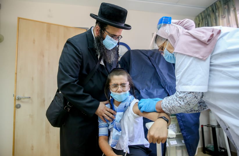 An ultra-Orthodox Jewish man and his child getting a flu vaccine at a health center in the northern Israeli city of Safed, October 22, 2020. (photo credit: DAVID COHEN/FLASH 90)
