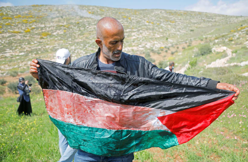 A man holds a Palestinian flag stained with blood of a mortally wounded Palestinian during a protest against Israeli settlements, in Beit Dajan in the Israeli-occupied West Bank March 19, 2021. (photo credit: REUTERS/RANEEN SAWAFTA)
