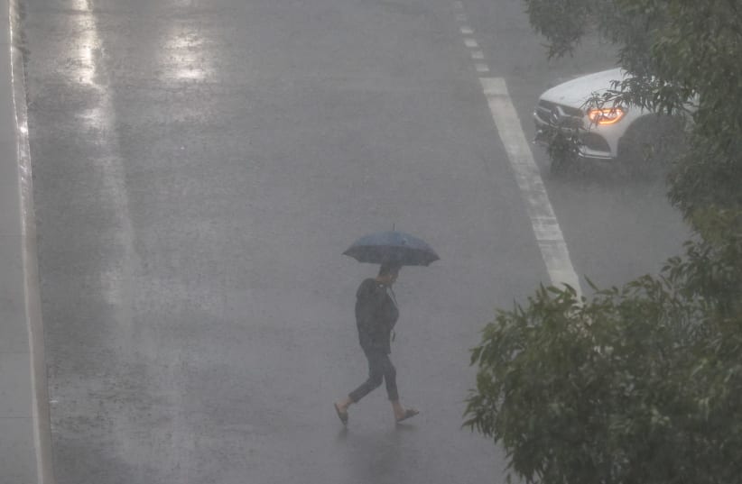 A person crosses a street in severe rain as the state of New South Wales experiences widespread flooding, in Sydney, Australia, March 20, 2021. (photo credit: LOREN ELLIOTT/REUTERS)