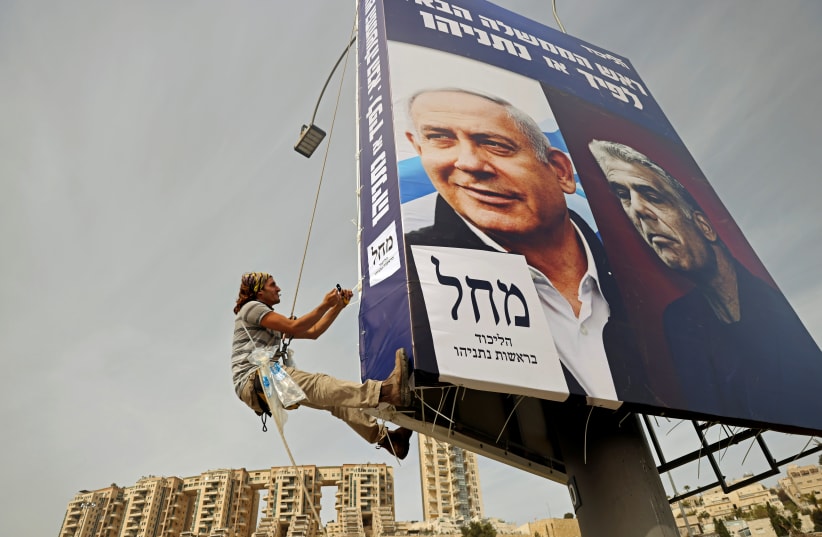 A man hangs a Likud election banner, depicting party leader Prime Minister Benjamin Netanyahu and his top challenger, Yesh Atid leader Yair Lapi (photo credit: RONEN ZVULUN/REUTERS)