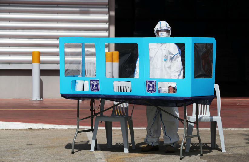 An employee wearing personal protective equipment stands behind a booth during a demonstration revealing preparations ahead of Israel’s upcoming election, at the Central Elections Committee’s logistics center in Shoham (photo credit: AMMAR AWAD / REUTERS)