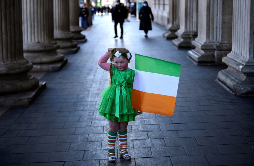 Willow O'Brien, 5, looks at her mother (not pictured) as she holds an Irish flag while posing for pictures, amid the outbreak of the coronavirus disease (COVID-19), on Saint Patrick's Day in Dublin, Ireland, March 17, 2021. (photo credit: CLODAGH KILCOYNE/REUTERS)
