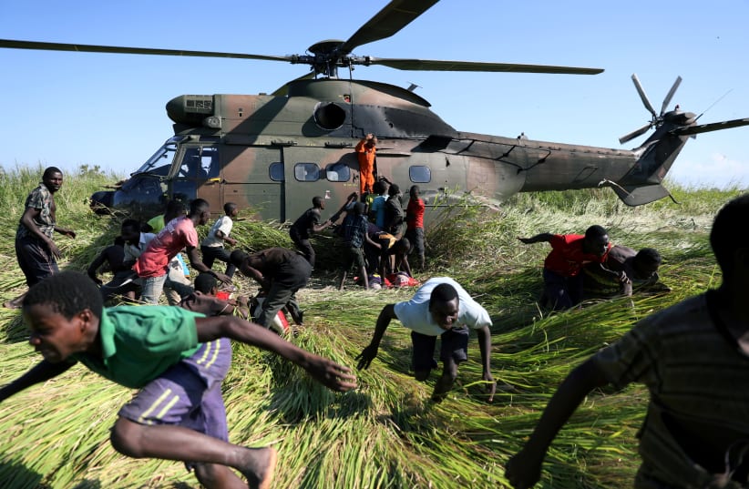 People run after collecting food aid from a South African National Defence Force (SANDF) helicopter in the aftermath of Cyclone Idai in Nhamatanda village, near Beira, Mozambique, March 26, 2019.  (photo credit: REUTERS/SIPHIWE SIBEKO)