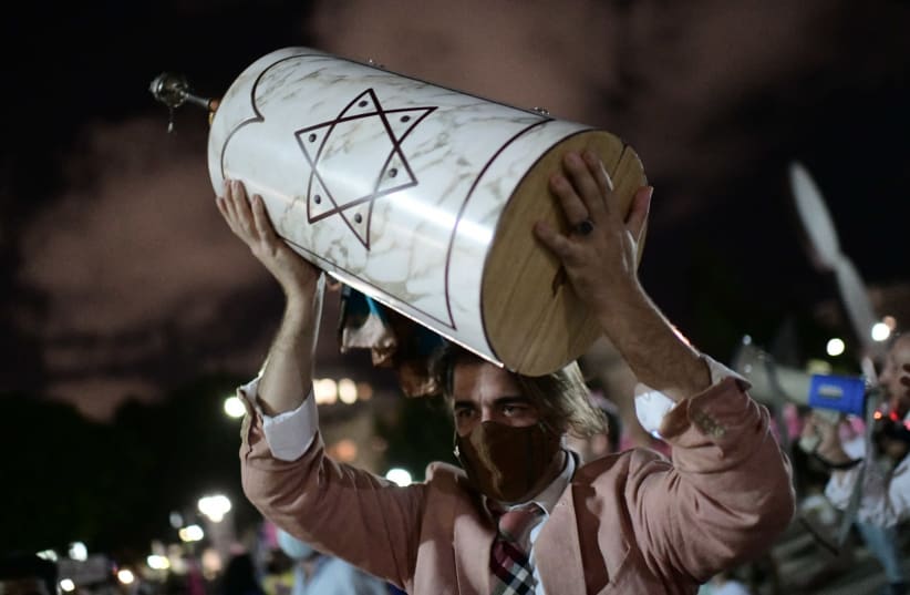 Israeli jews dance as they hold a Scroll of a Torah during Simhat Torah celebrations at Habima Square, Tel Aviv. The worshippers are marking the end of the annual cycle of the reading of the Torah and the beginning of the next cycle. October 10, 2020. Photo by Tomer Neuberg/Flash90 (photo credit: REUTERS/TOMER NEUBERG/FLASH90)