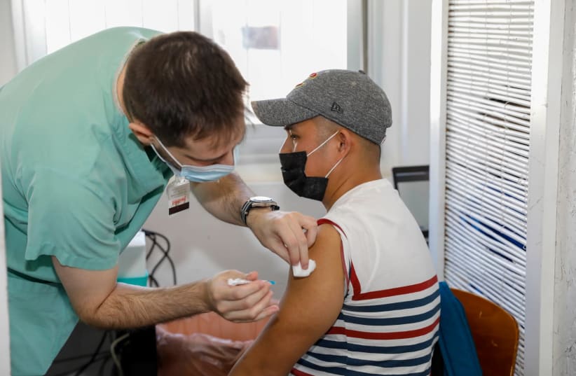 A worker at the south Tel Aviv vaccination center administers the coronavirus vaccine to a foreign national. (photo credit: GUY YECHIELY)