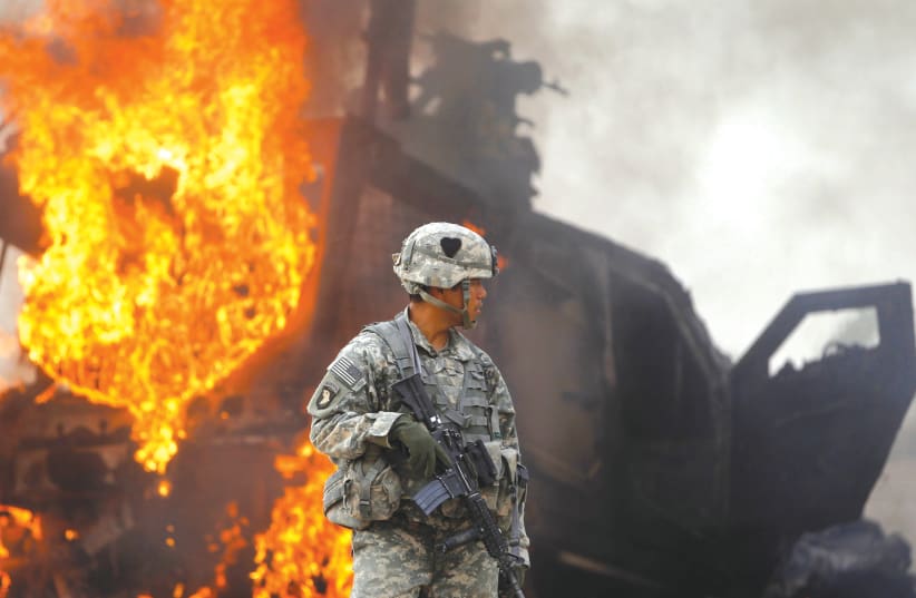 CAPTAIN MELVIN CABEBE with the US Army’s 1-320 Field Artillery Regiment, 101st Airborne Division stands near a burning M-ATV armored vehicle after it struck an improvised explosive device (IED) near Combat Outpost Nolen in the Arghandab Valley north of Kandahar, Afghanistan, in 2010. (photo credit: BOB STRONG / REUTERS)