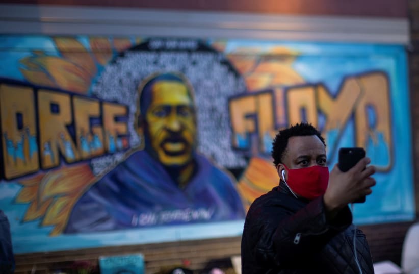 A local resident takes a selfie in front of a mural of George Floyd after the verdict in the trial of former Minneapolis police officer Derek Chauvin, found guilty of the death of George Floyd, at George Floyd Square in Minneapolis, Minnesota, US, April 20, 2021. (photo credit: REUTERS/CARLOS BARRIA)