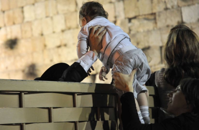 PASSING A baby over the Kotel mechitza. Here in Israel, passersby will give mothers unsolicited advice about their children (photo credit: SOPHIE GORDON/FLASH90)