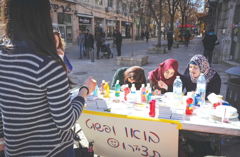 Muslim young women participate in a project by Bezalel art students inviting people on the street to draw themselves, in central Jerusalem, in 2017. (photo credit: NATI SHOHAT/FLASH90)