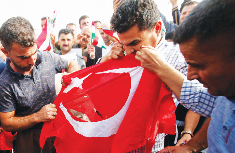 IRAQI KURDS tear the Turkish flag during a demonstration against Turkey’s incursion in Syria, outside the UN building in Erbil. (photo credit: AZAD LASHKARI / REUTERS)