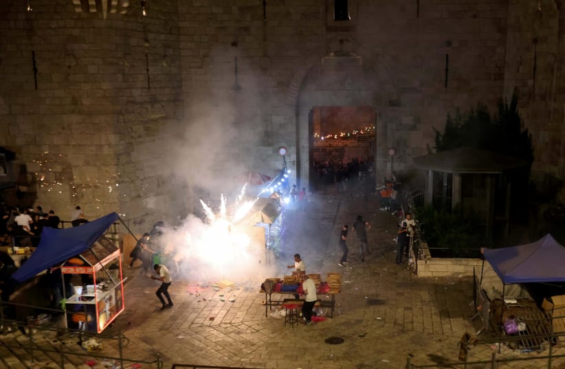 Palestinians react to a stun grenade fired by Israeli police during clashes at Damascus Gate on Laylat al-Qadr during the holy month of Ramadan, in Jerusalem's Old City, May 9, 2021. (photo credit: RONEN ZVULUN/REUTERS)