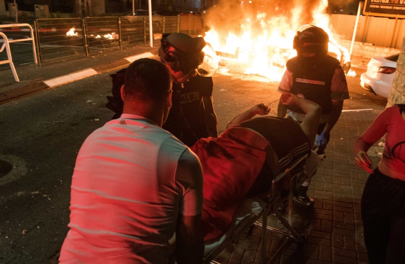 Medics evacuate an injured man during clashes between Arab and Jews in Acre, northern Israel, May 12, 2021.  (photo credit: RONI OFER/FLASH90)
