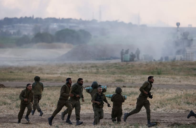 Israeli soldiers carry artillery shells and run in a field near the border between Israel and the Gaza Strip, on its Israeli side May 17, 2021. (photo credit: REUTERS/AMIR COHEN)