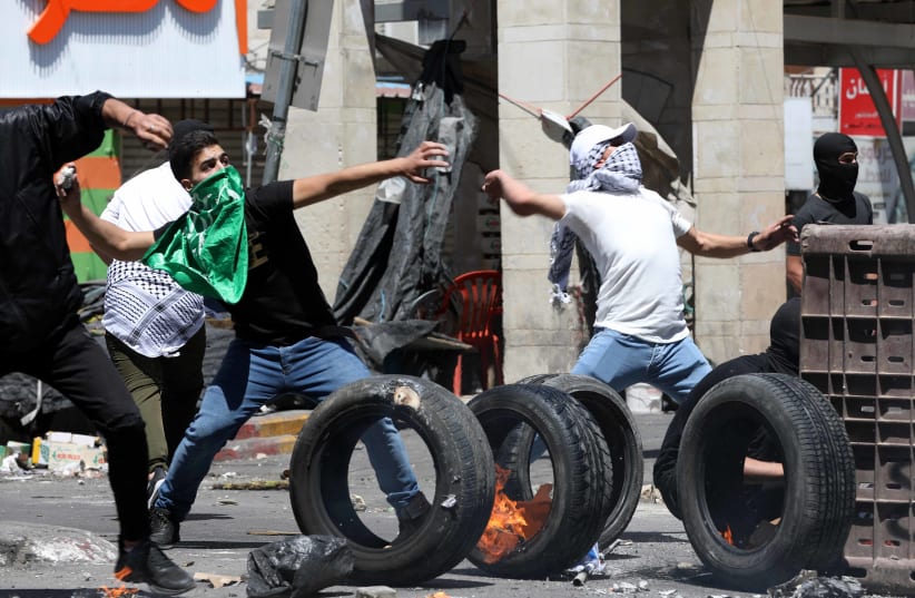 Palestinian youth clash with Israeli security forces in the West Bank city of Hebron, May 14, 2021 (photo credit: WISAM HASHLAMOUN/FLASH90)