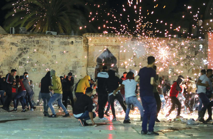 DEMONSTRATORS REACT as Israeli police fire stun grenades during clashes at the compound that houses al-Aqsa Mosque, in Jerusalem’s Old City on May 7. (photo credit: AMMAR AWAD/REUTERS)
