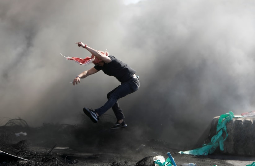 A Palestinian jumps next to a barricade made with tires during an anti-Israel protest over a cross-border violence between Palestinian militants in Gaza and the Israeli military, near Hawara checkpoint near Nablus in the West Bank, May 18, 2021. (photo credit: RANEEN SAWAFTA/ REUTERS)