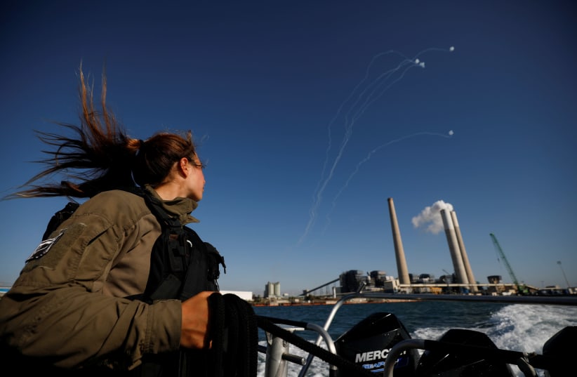 An Israeli soldier looks on as Israel's Iron Dome anti-missile system intercept rockets launched from the Gaza Strip towards Israel, as it seen from a naval boat patrolling the Mediterranean Sea off the southern Israeli coast as Israel-Gaza fighting rages on May 19, 2021. (photo credit: AMIR COHEN/REUTERS)