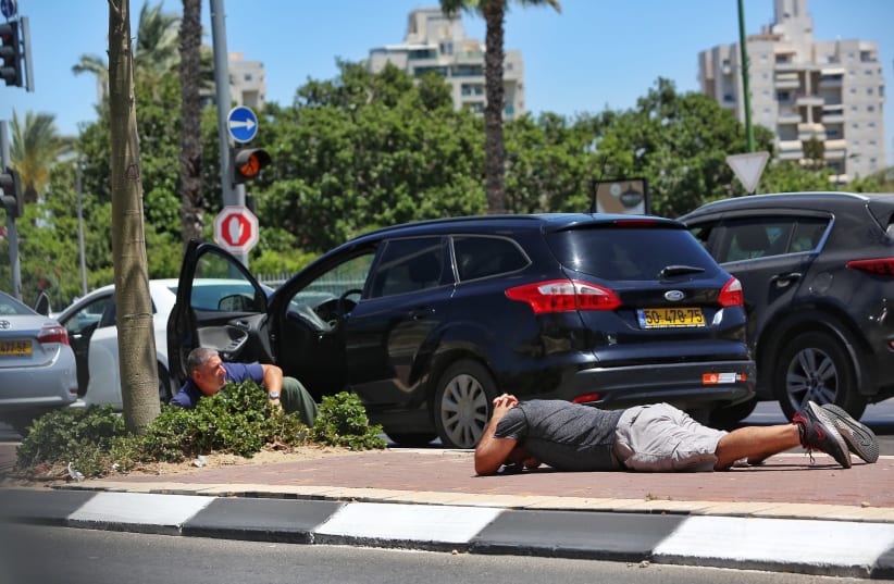 Israelis take cover as a siren sounds a warning of incoming rockets fired from the Gaza strip in the city of Ashkelon, southern Israel, on May 19, 2021. (photo credit: EDI ISRAEL/FLASH90)