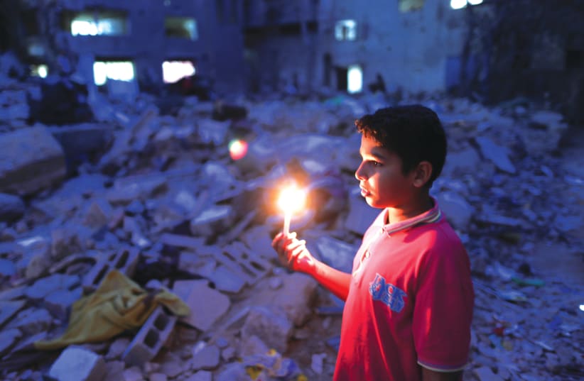 A BOY holds a candle at the site of a house that was destroyed by Israeli airstrikes during the Israeli-Palestinian fighting, in Gaza earlier this week. (photo credit: SUHAIB SALEM/REUTERS)