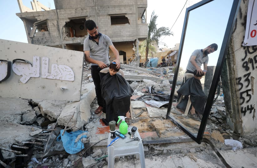 A barber works amid rubble of his shop, which was destroyed in an Israeli airstrike during Israeli-Palestinian fighting, in Gaza City May 25, 2021. (photo credit: MOHAMMED SALEM/REUTERS)