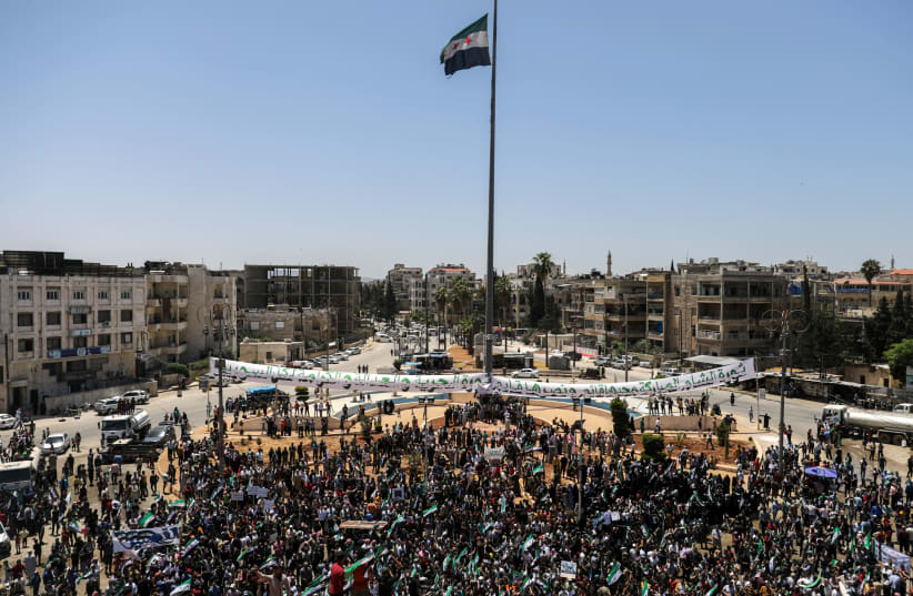 An opposition flag flies as people gather during a demonstration against Syria's President Bashar Assad and presidential elections, in the opposition-held Idlib, Syria May 26, 2021. (photo credit: KHALIL ASHAWI / REUTERS)