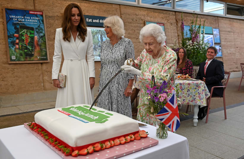 Britain's Queen Elizabeth attempts to cut a cake with a sword next to Camilla, Duchess of Cornwall, and Catherine, Duchess of Cambridge as they attend a drinks reception on the sidelines of the G7 summit, at the Eden Project in Cornwall, Britain June 11, 2021 (photo credit: OLI SCARFF/POOL VIA REUTERS)