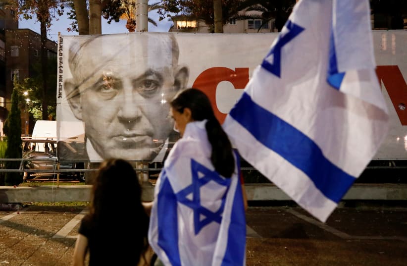 People walk in front of a picture of former Prime Minister Benjamin Netanyahu after Israel's parliament voted in a new coalition government, ending Netanyahu's 12-year hold on power, in Tel Aviv, Israel June 13, 2021. (photo credit: REUTERS/CORINNA KERN)
