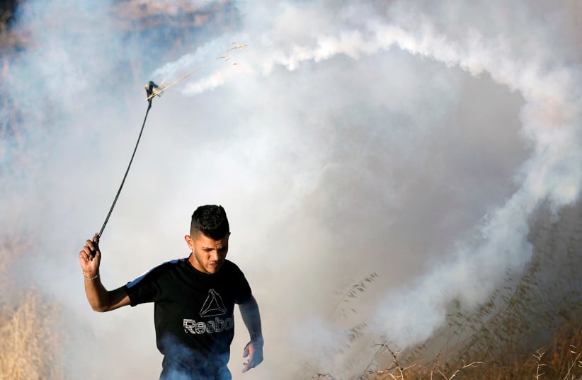 A Palestinian demonstrator uses a sling to hurl back a tear gas canister fired by Israeli forces during a protest over a Jerusalem flag-waving procession by far-right Israeli groups, near the West Bank Jewish settlement of Beit El near Ramallah. June 15, 2021 (photo credit: MOHAMAD TOROKMAN/REUTERS)