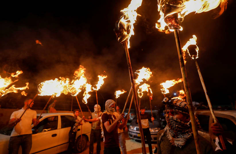 Palestinian demonstrators hold torches during a night protest against Israeli settlements in Beita in the Israeli-occupied West Bank, June 22, 2021 (photo credit: MOHAMAD TOROKMAN/REUTERS)
