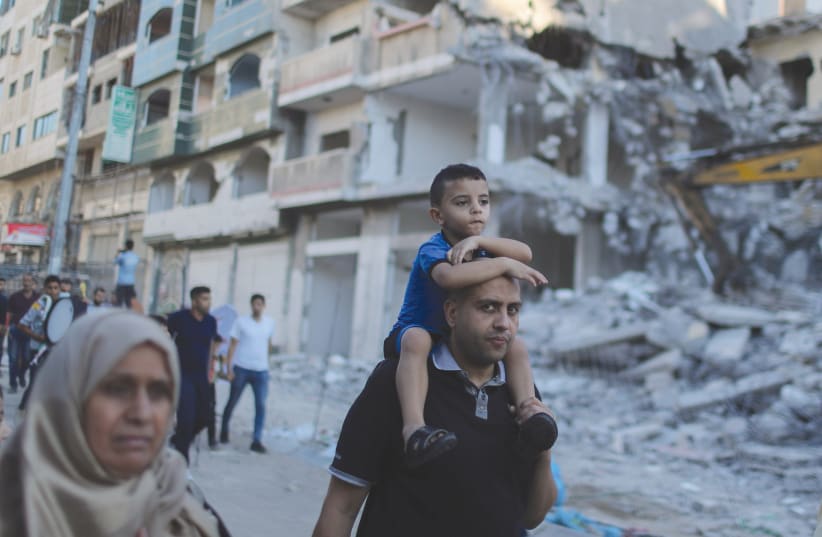PALESTINIANS WALK past destroyed apartment buildings in Gaza earlier this month. (photo credit: MOHAMMED SALEM/ REUTERS)