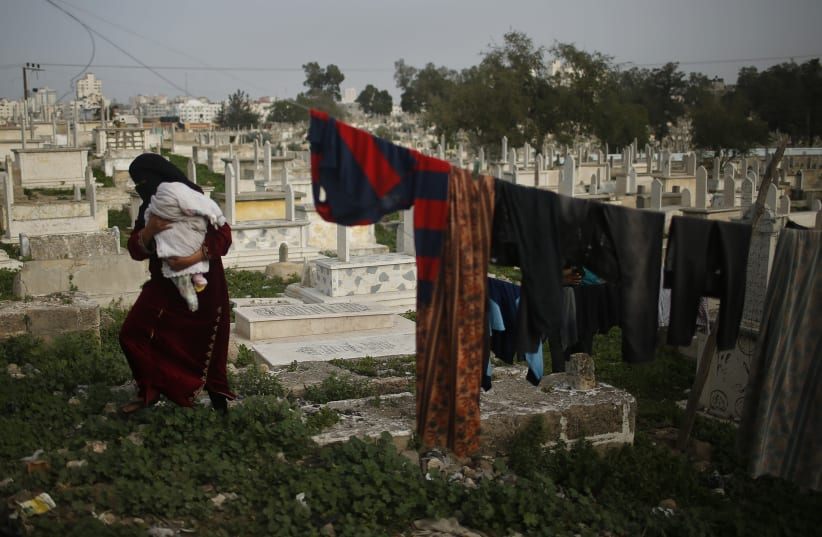 A Palestinian woman, who lives in Sheikh Shaban cemetery, walks amongst graves in Gaza City. (photo credit: REUTERS/MOHAMMED SALEM)