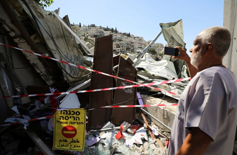A Palestinian man uses his mobile phone as he stands near the debris of a shop that Israel demolished in the Palestinian neighbourhood of Silwan in East Jerusalem June 29, 2021 (photo credit: AMMAR AWAD / REUTERS)