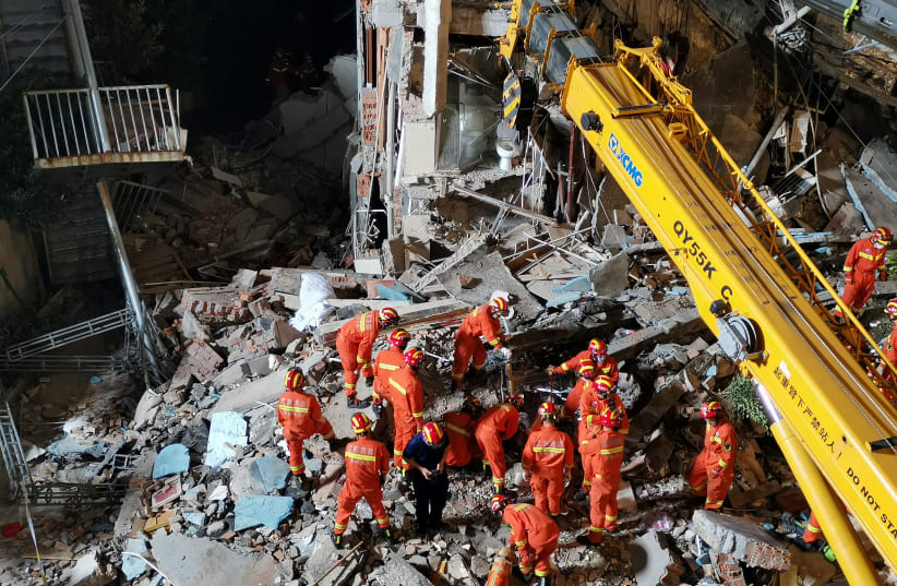 Rescue workers work next to a crane at the site where a hotel building collapsed in Suzhou, Jiangsu province, China July 12, 2021.  (photo credit: CNSPHOTO VIA REUTERS)