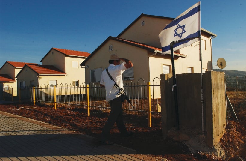 AN ARMED MAN looks at the Israeli flag in the settlement of Rehelim in 2002, whose founders included now-Peace Now activist Shabtay Bendet.  (photo credit: FLASH90)