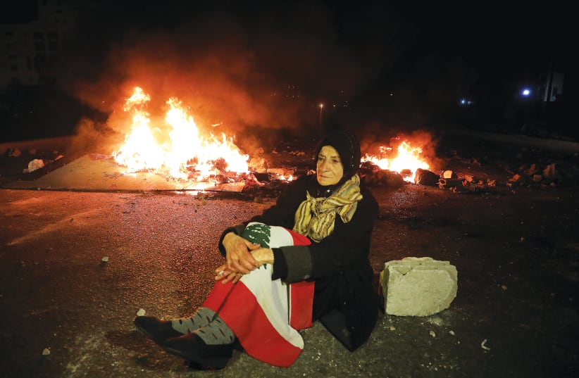 A WOMAN sits near a fire during a protest in March in Beirut against the fall in the Lebanese currency and mounting economic hardship. (photo credit: MOHAMED AZAKIR/REUTERS)