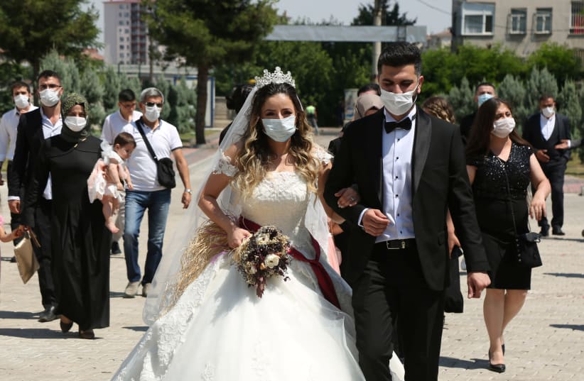 A bride and groom walk to their wedding in face masks amid the coronavirus pandemic (photo credit: REUTERS/SERTAC KAYAR)