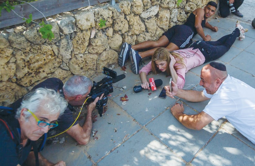 PEOPLE TAKE cover as sirens warn of incoming rockets fired at Ashkelon from Gaza in May.  (photo credit: EDI ISRAEL/FLASH90)