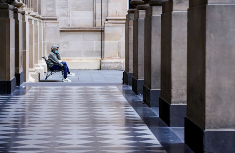 A lone man wearing a protective face mask sits at an unusually quiet State Library on the first day of a lockdown as the state of Victoria looks to curb the spread of a coronavirus disease (COVID-19) outbreak in Melbourne, Australia, July 16, 2021. (photo credit: REUTERS/SANDRA SANDERS/FILE PHOTO)