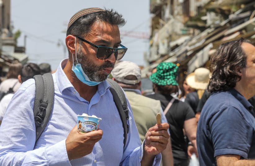 A man eating Ben & Jerry's ice cream in Mahaneh Yehuda in Jerusalem, July 20, 2021.  (photo credit: MARC ISRAEL SELLEM/THE JERUSALEM POST)